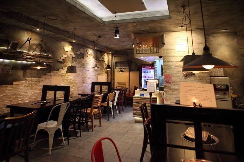 Interiors of Hwa Tteok restaurant in Myeongdong, Seoul, presenting a rustic and warmly lit setting with empty tables awaiting customers.